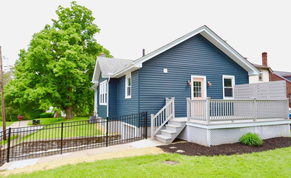 A black ornamental aluminum fence running along the front walk of a blue-sided house, with white porch railings and a clipped green lawn.