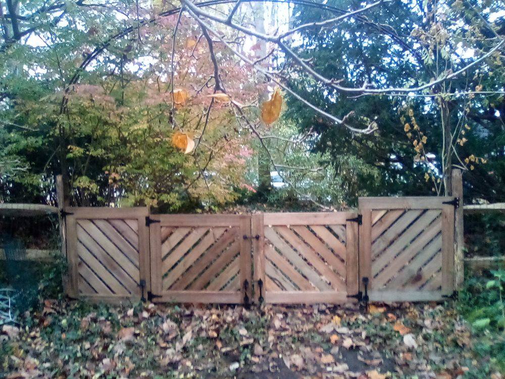 A pair of tall wooden gates in a lattice-topped board fence, set in a back yard thick with fallen autumn leaves.